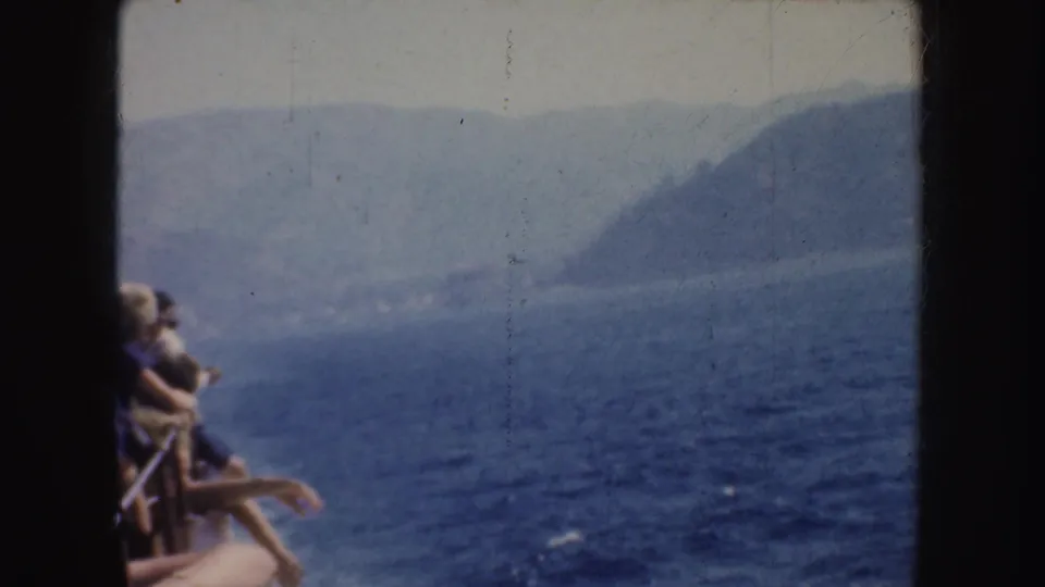 1952 California 8mm frame with a partial seated passenger, open water, and hazy coastal hills in the distance.