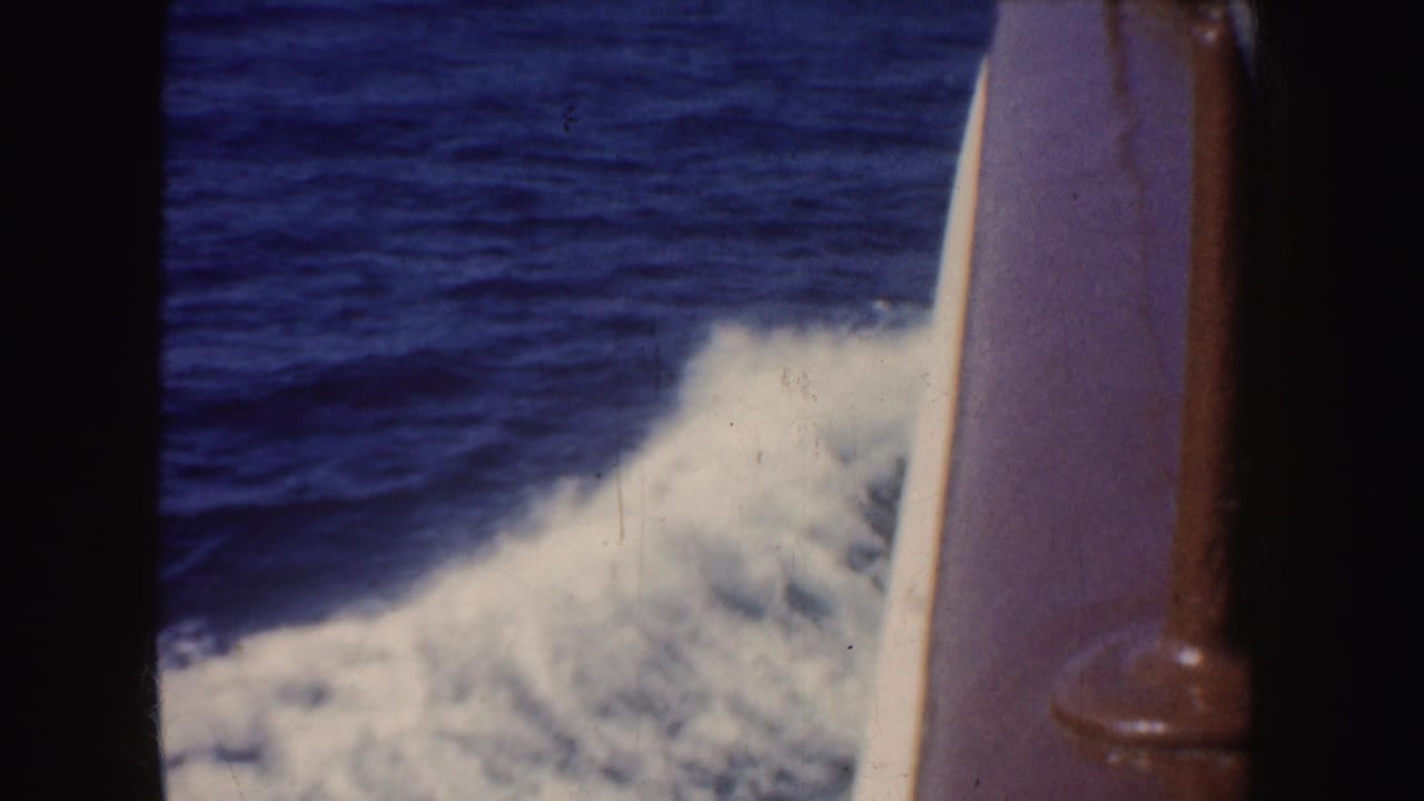 1952 California 8mm frame showing blue ocean and white wake viewed through a dark boat window beside a brown rail.