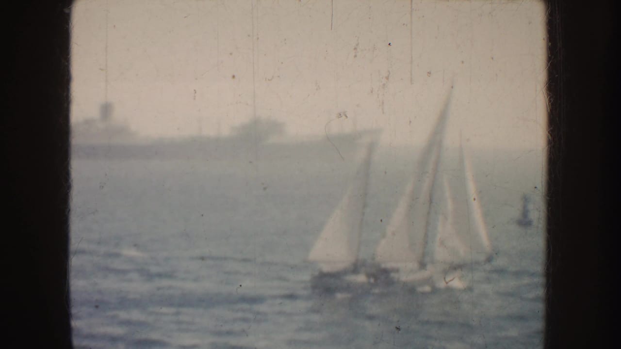 Two white sailboats on hazy water with a large ship in the distance.