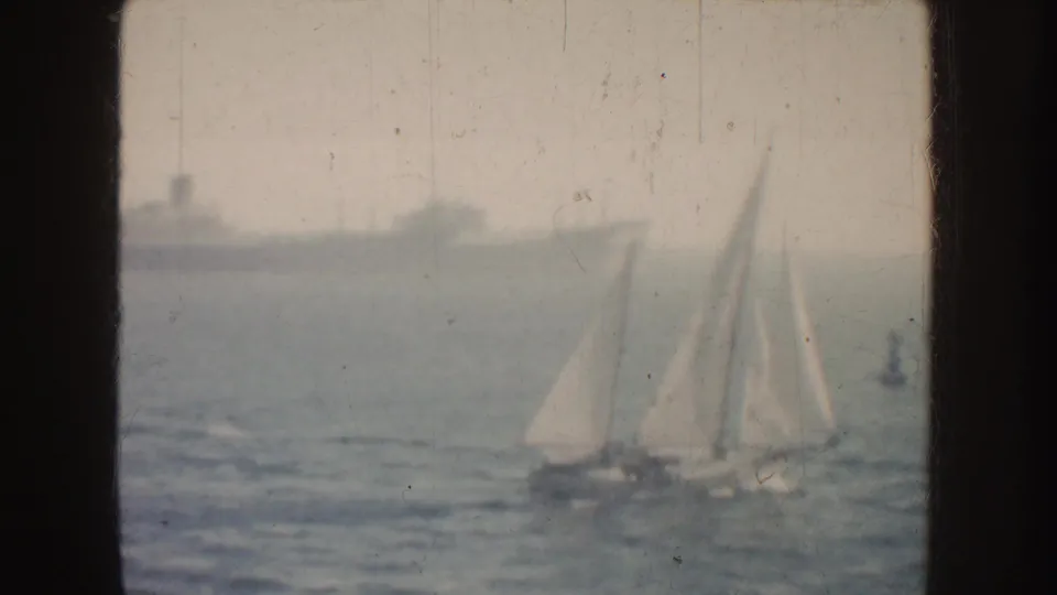 1952 California 8mm frame showing white sailboats on hazy blue water with a large grey ship beyond them.