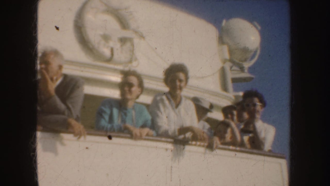Adults stand at a white ship balcony rail under bright sun.