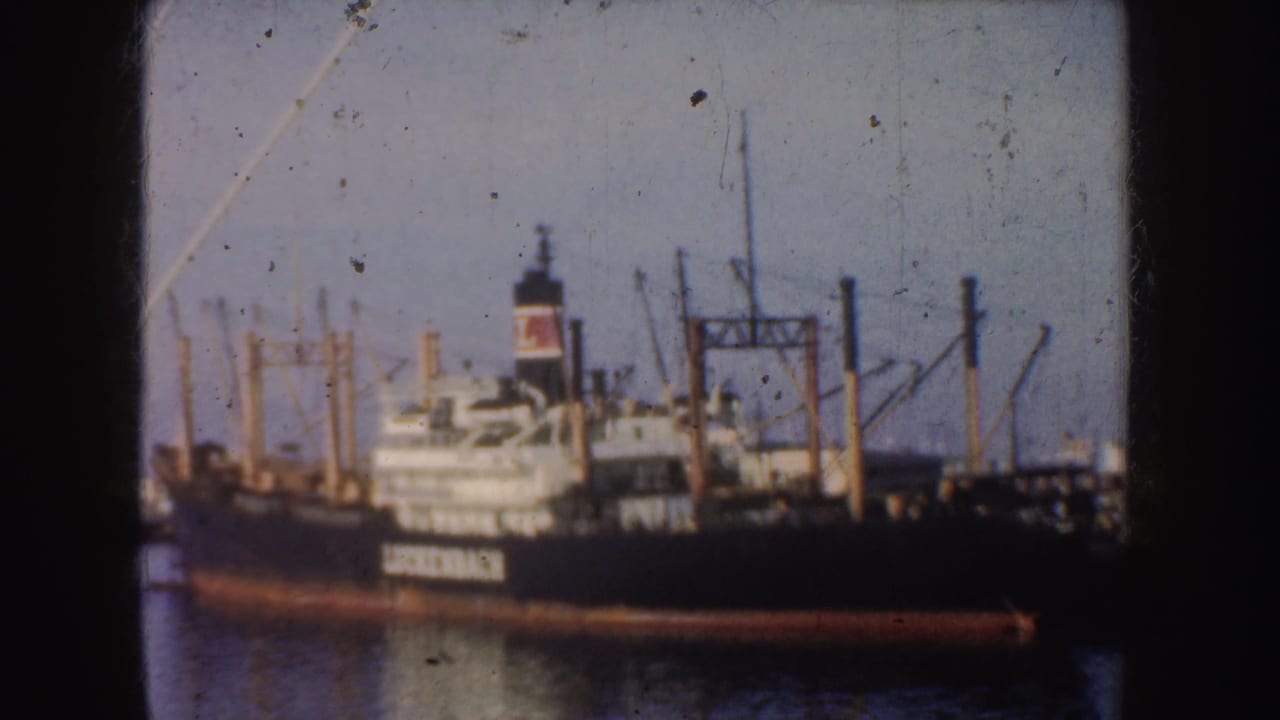 1952 California harbor view of a black Luckenbach cargo ship with a red-and-white funnel and port cranes in the background.
