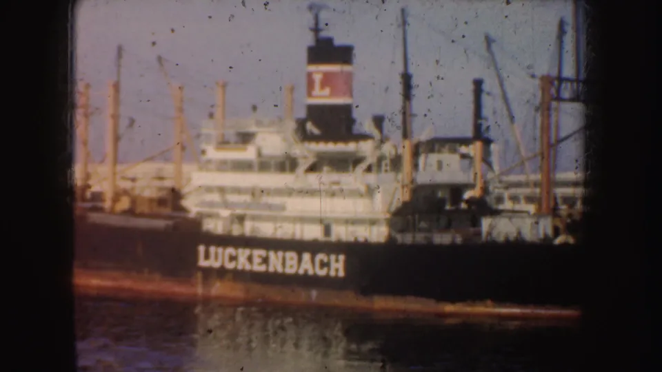 Closer 1952 California harbor frame showing the Luckenbach name on the hull, the marked funnel, deck structures, and nearby port equipment.