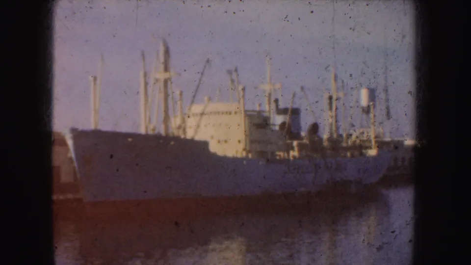 1952 California harbor view of a light-colored cargo ship or freighter with multiple masts, seen softly across the water.