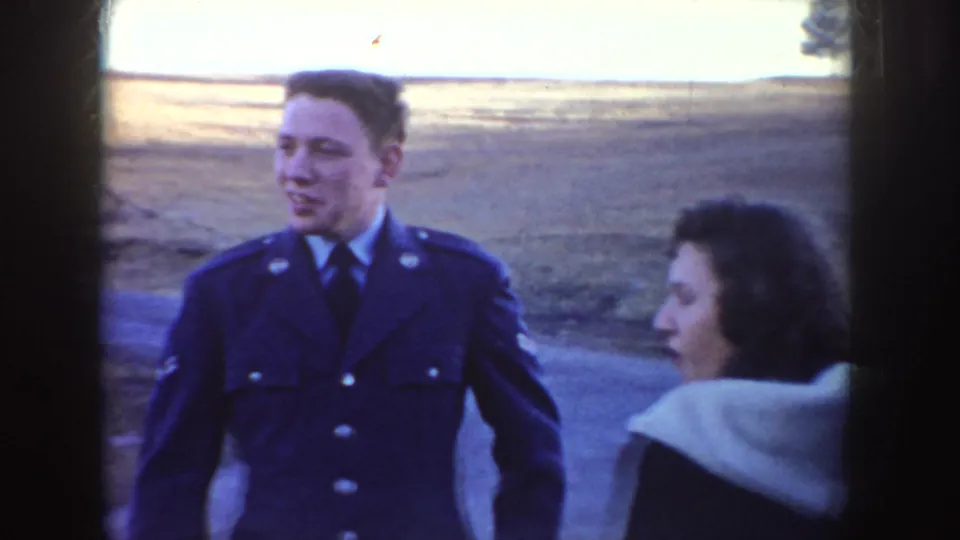 A young man in a military-style uniform walks with a woman near a road in 1955 Idaho home-movie footage.