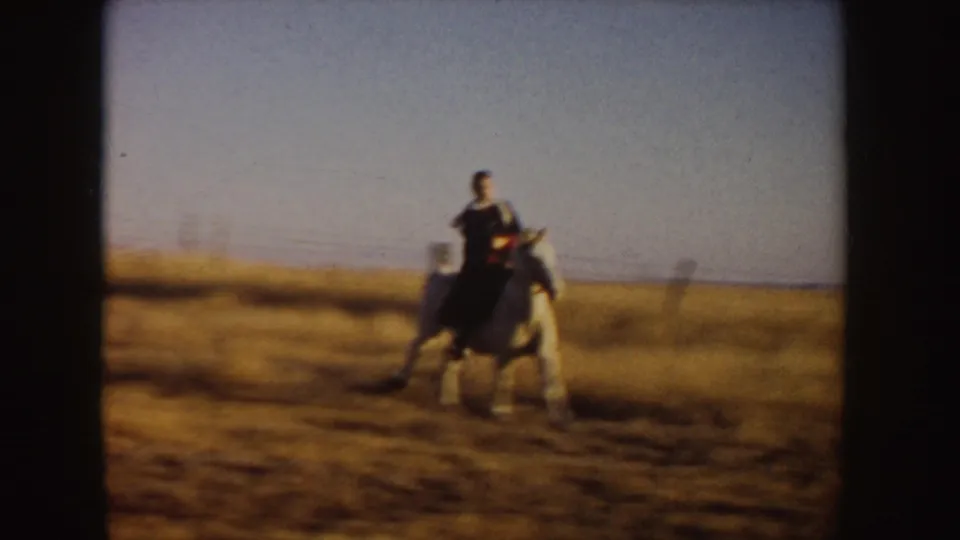 A woman rides a light-colored horse across the 1955 Idaho prairie, with motion blur from the moving 8mm camera.