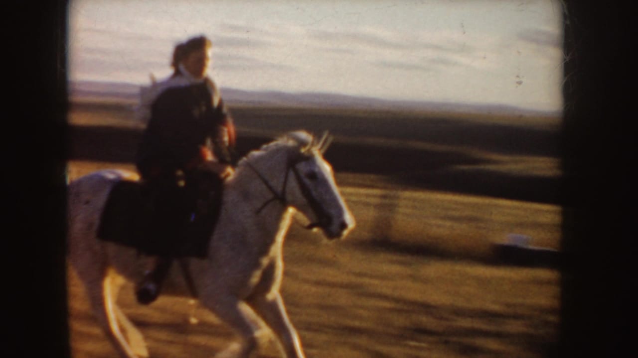 1955 Idaho 8mm frame showing a rider in dark clothing on a white horse crossing open plains in warm light.