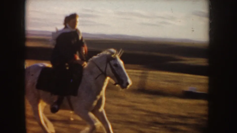 1955 Idaho 8mm frame showing a rider in dark clothing on a white horse crossing open plains in warm light.
