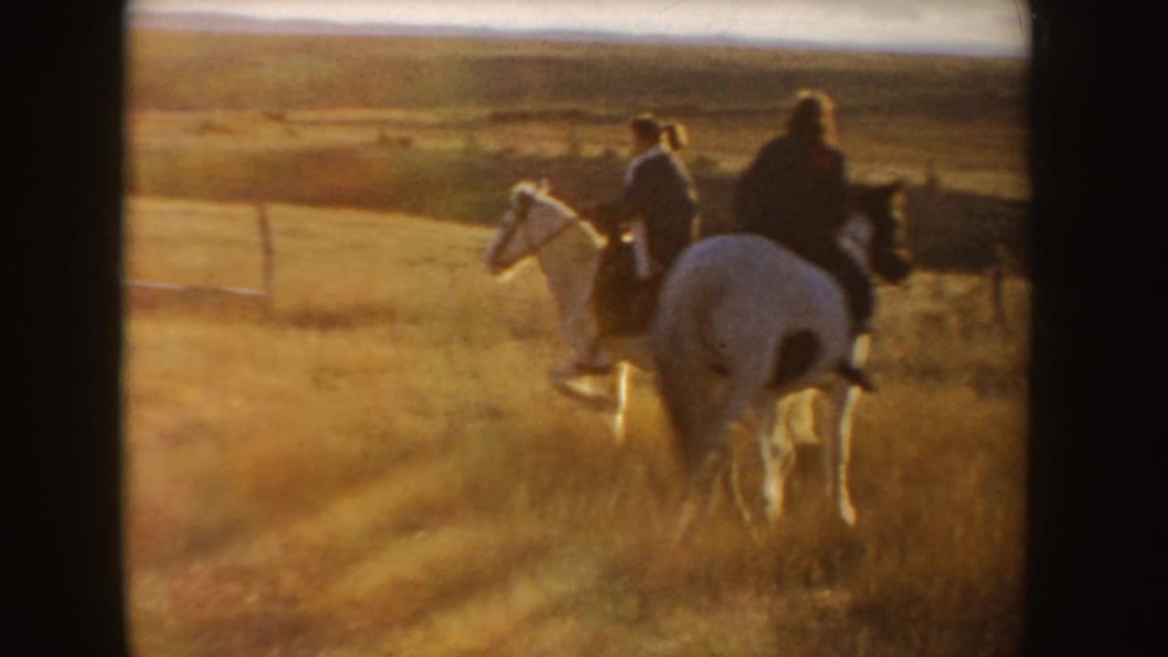 1955 Idaho 8mm frame showing riders moving away on horses across a dry golden field in late-day light.