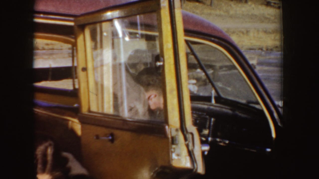 Man seated in the front of a classic car seen through the open door and window.