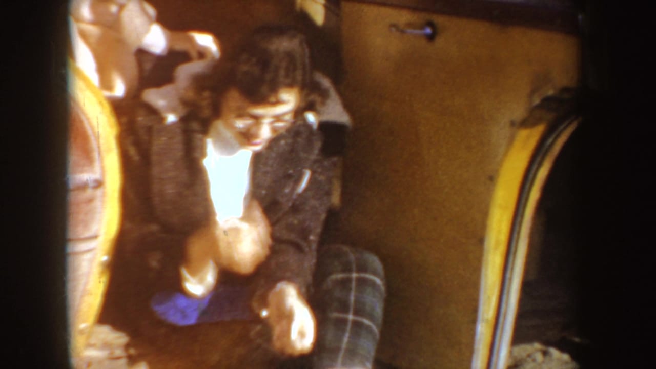 Woman in a dark coat sits inside a car and looks down while adjusting something near her lap.