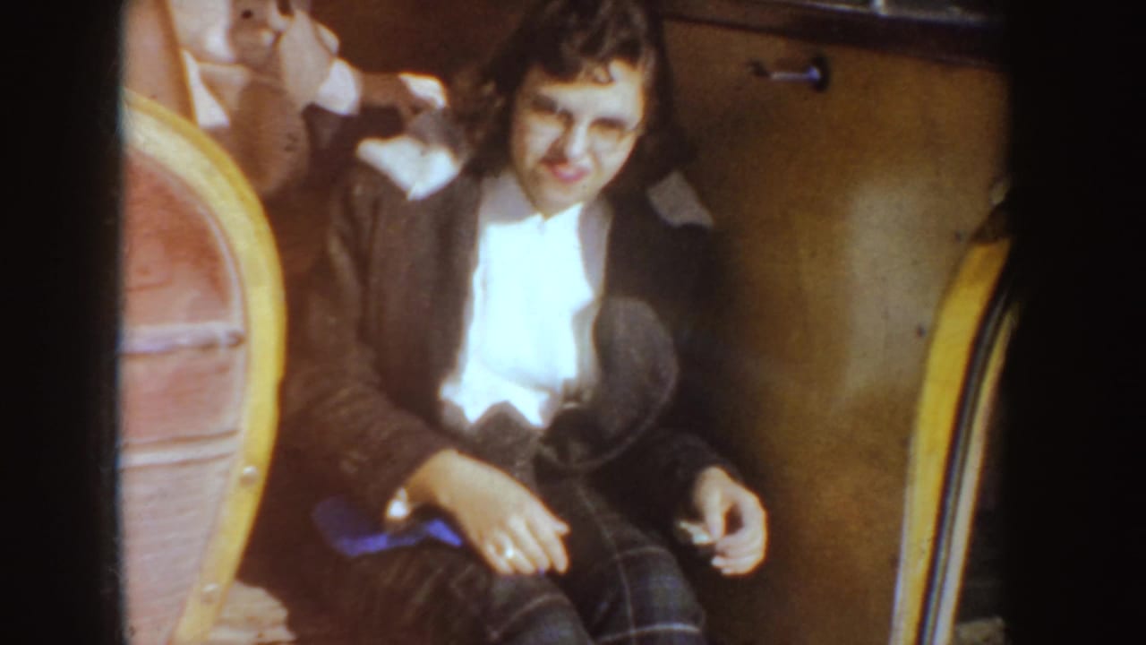 Woman in a dark coat smiles from the passenger area of a car with a rounded seat beside her.