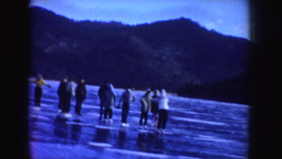 A group of people appears on a frozen Idaho lake under a blue twilight sky, with wooded hills beyond the ice.