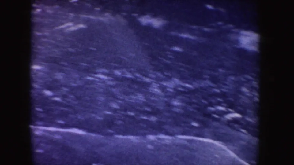 1955 Idaho home-movie frame with dark icy ground and a pale snow or ice line across the lower area.