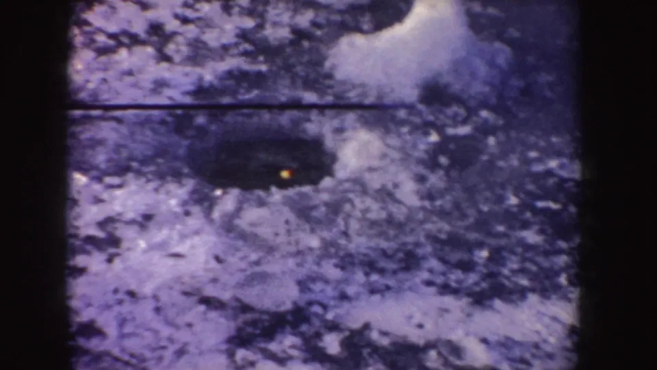 1955 Idaho 8mm frame showing snow-covered ground around a dark opening with a faint yellow light visible within it.