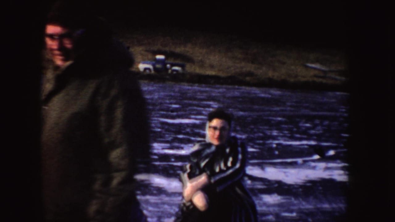 Two people on a frozen lake, with one person close to camera and another crouched on the ice.