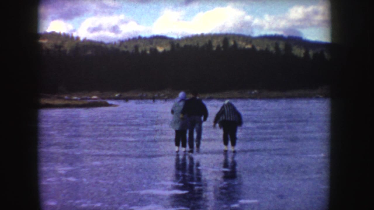 Four bundled people move across a frozen pond with forested hills behind them.