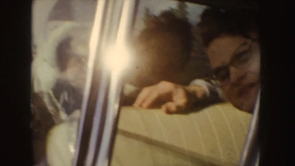 Close 1955 home-movie view of a person by a car window, with glare, soft focus, and vehicle interior details visible.