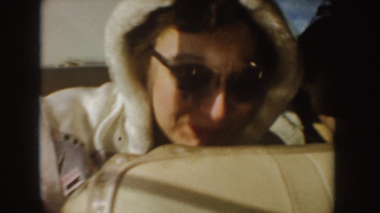 A woman in sunglasses and a white hooded jacket smiles from the back seat of a car in the Idaho road-trip footage.