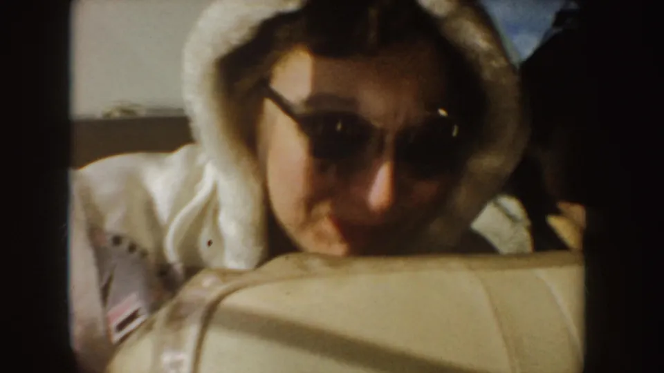 A woman in sunglasses and a white hooded jacket smiles from the back seat of a car in the Idaho road-trip footage.