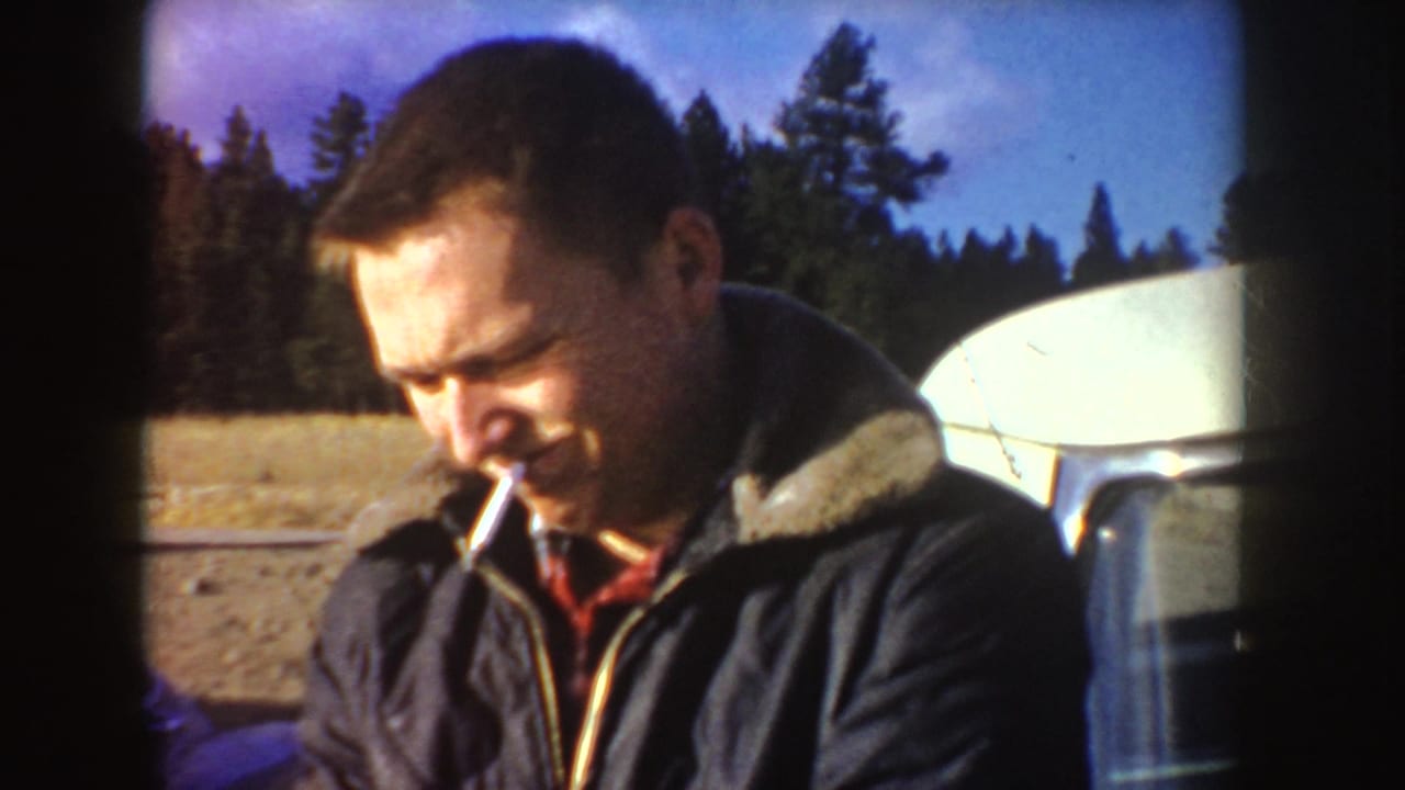 In daylight Idaho footage, the same adult man appears to smoke a cigarette outdoors with trees, open ground, and camper equipment behind him.