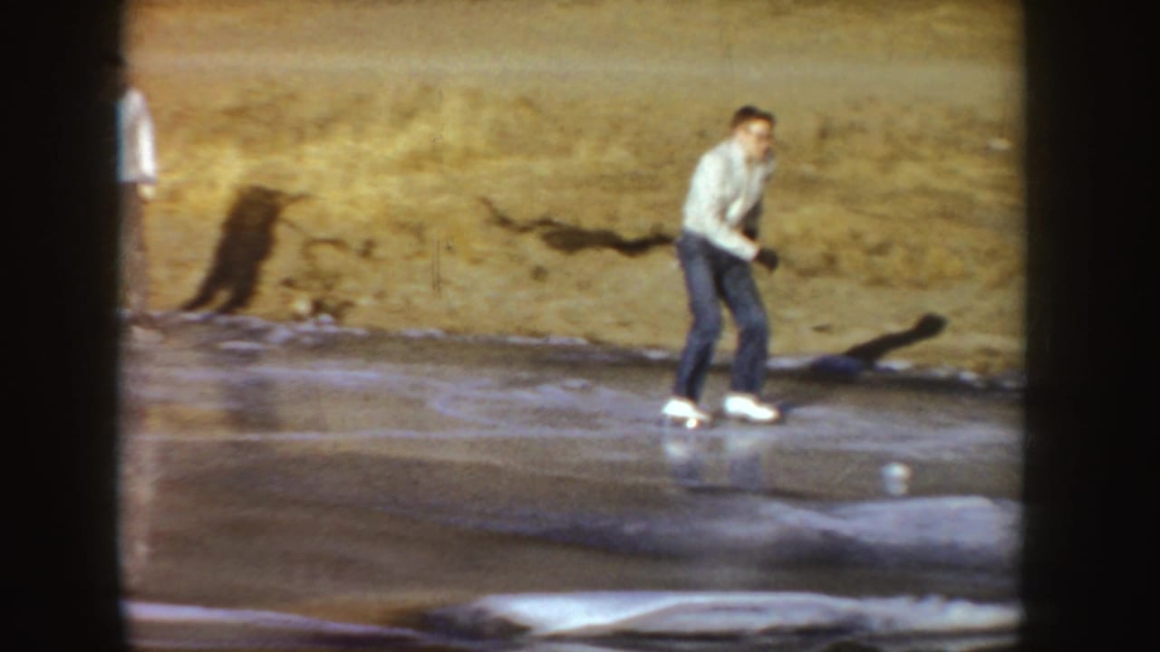 Young man in a light top and jeans skates across outdoor ice in Idaho home-movie footage from 1955.