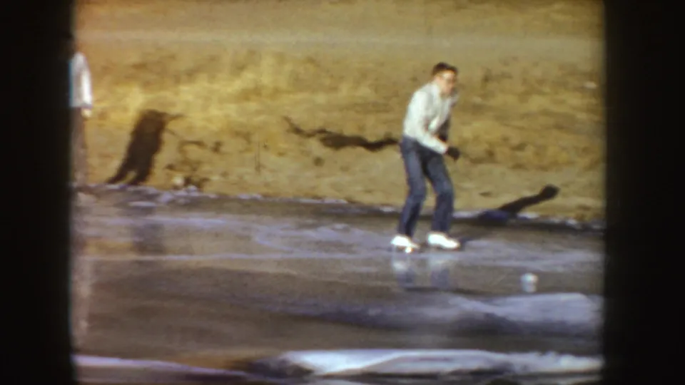 Young man in a light top and jeans skates across outdoor ice in Idaho home-movie footage from 1955.