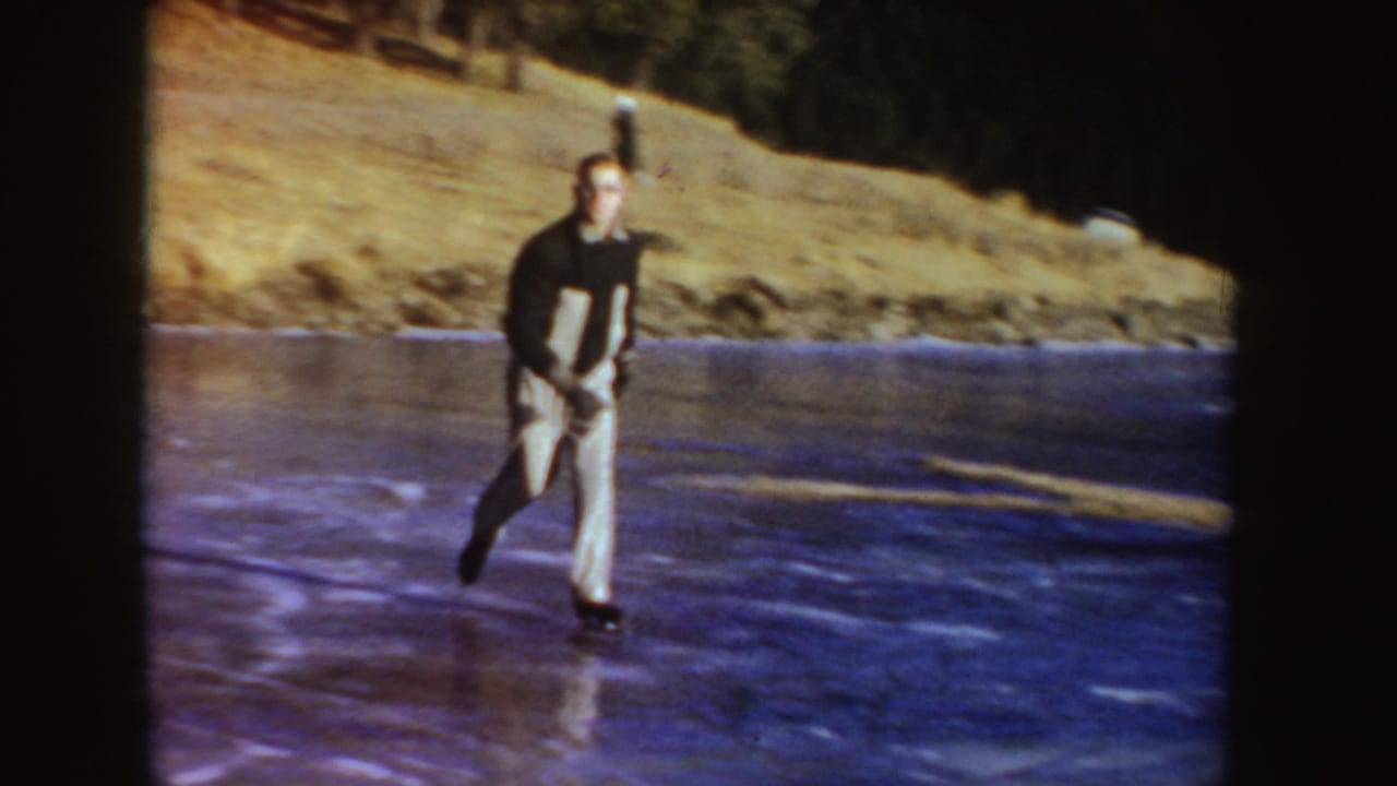 Man skating on a frozen pond beside a grassy bank.