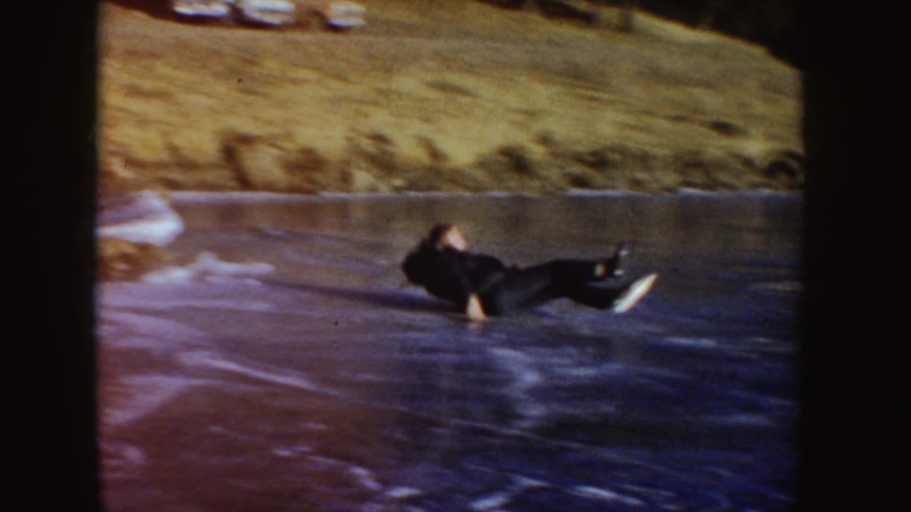 The home movie shows a skater on their back on the frozen pond, with the grassy shoreline visible behind them.