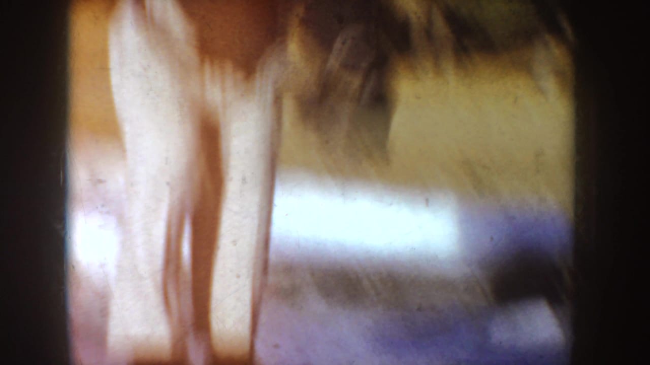 Blurred close view of a person skating on ice with dark clothing and light pants.