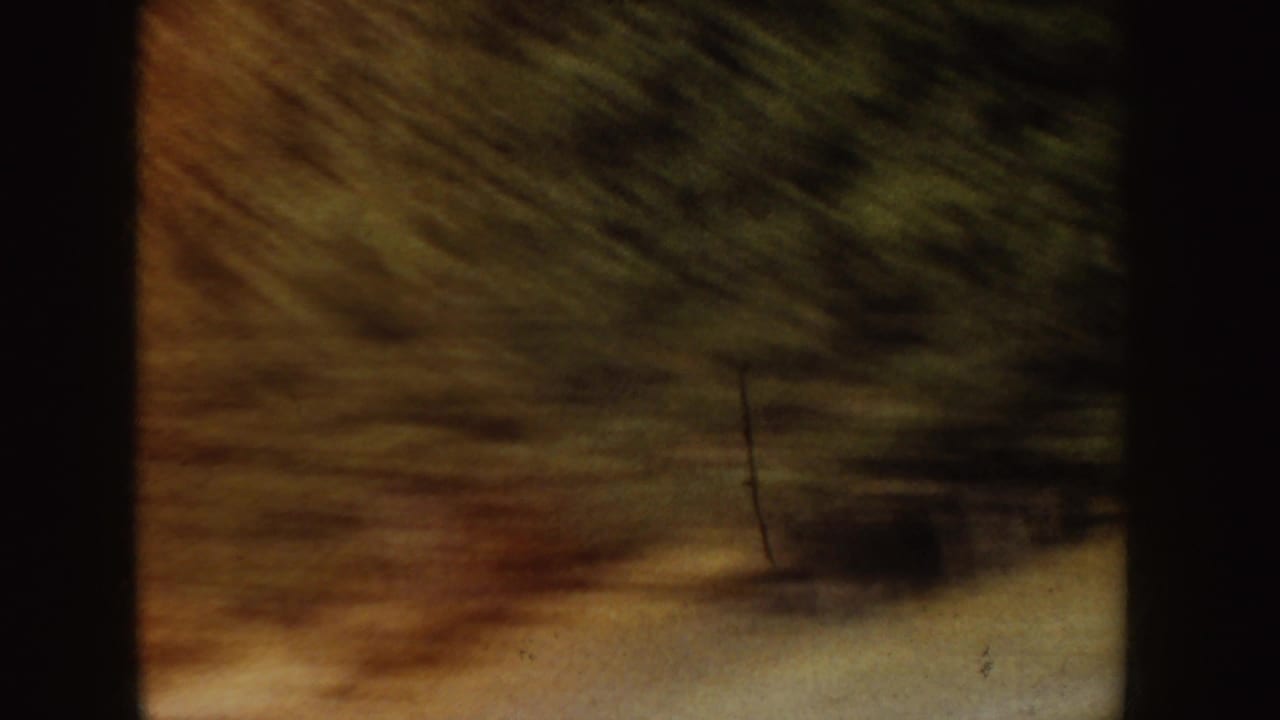 Archival 8mm frame of the frozen pond surface with dark tree shadows and heavy handheld cropping.