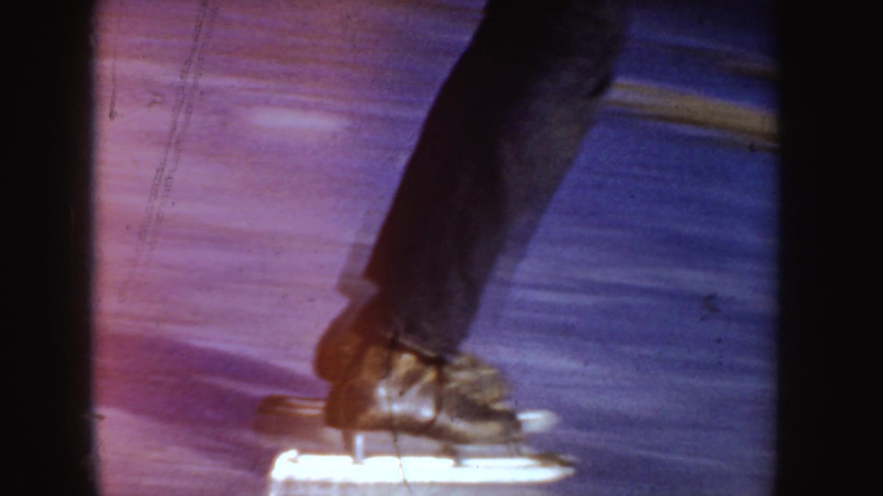 Close 8mm view of skating boots and blades crossing the frozen surface in the 1955 Idaho home movie.