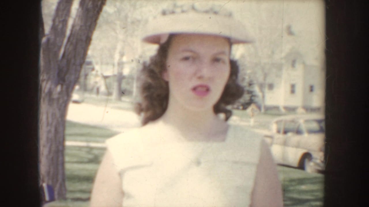 Young woman in a white dress and hat walking on a tree-lined sidewalk.