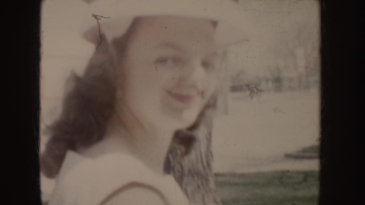 Soft, close 8mm view of a young woman in a white hat and dress looking toward the camera outdoors in Idaho, 1955.