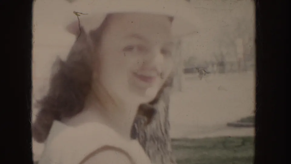 Soft, close 8mm view of a young woman in a white hat and dress looking toward the camera outdoors in Idaho, 1955.