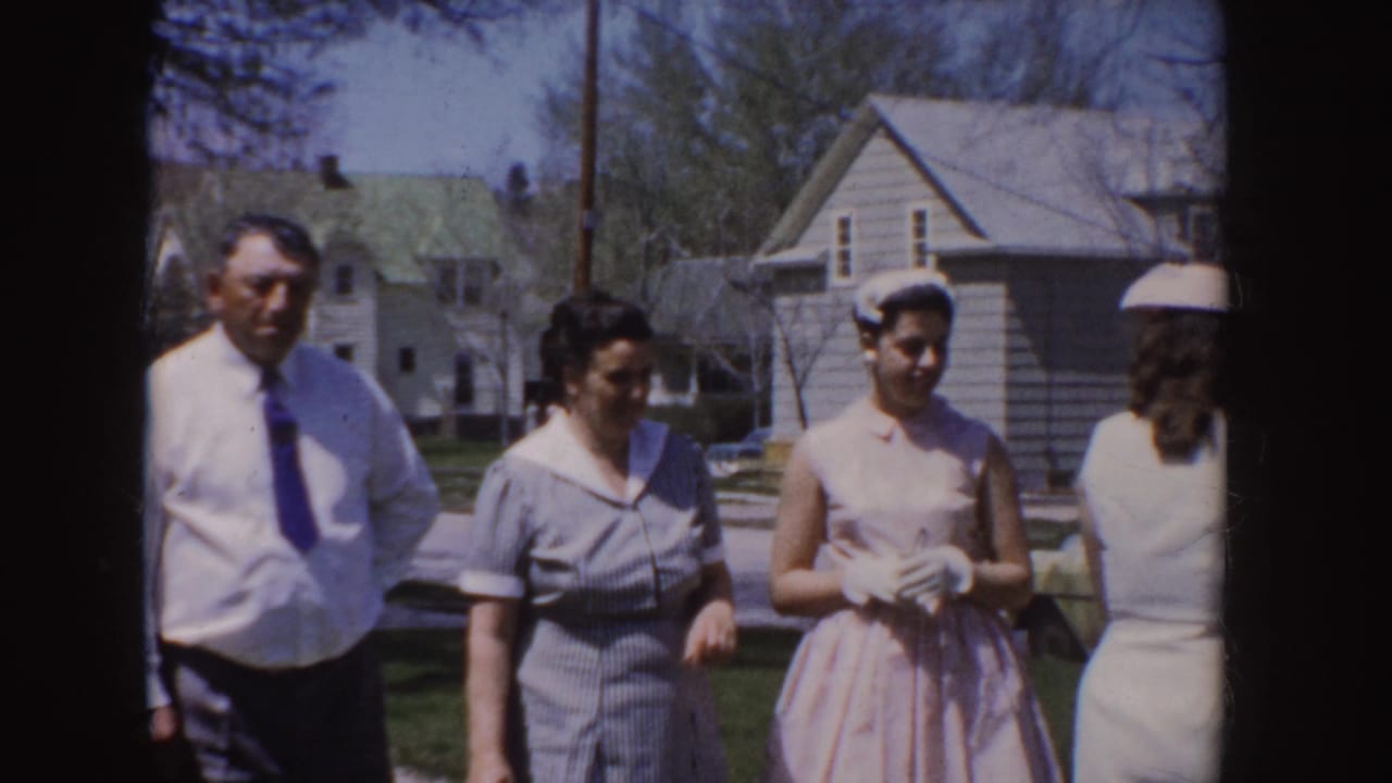 Man in white shirt and tie stands with women in dresses on a sunny lawn.