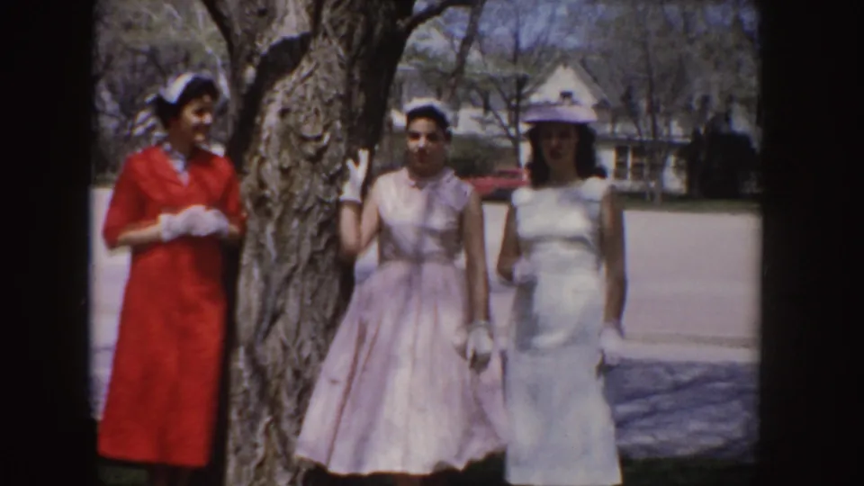 The women continue posing in their formal 1950s attire beside a large tree in a residential Idaho setting.