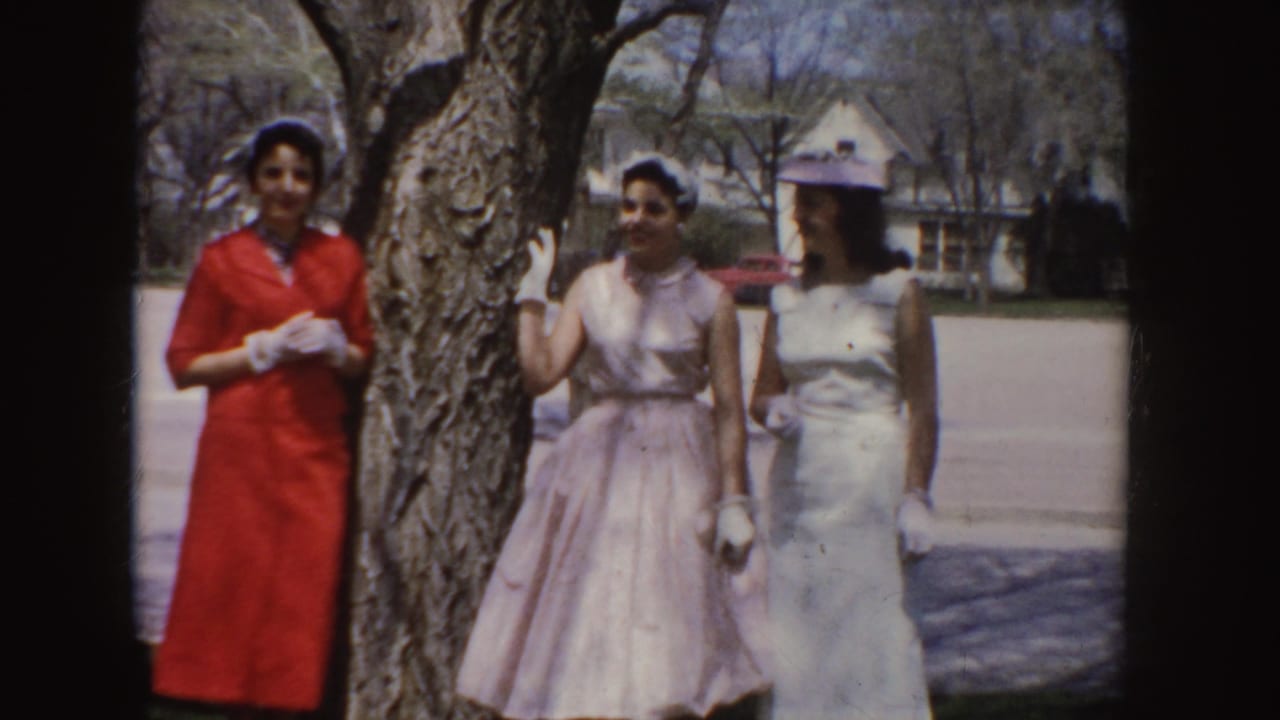 Three women in red, pink, and white dresses pose beside a tree outdoors.