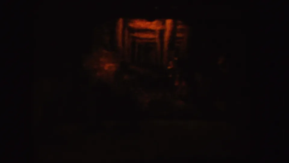 The final frame holds on the dimly lit wooden structure, with warm highlights and dense shadows typical of low-light 8mm footage.