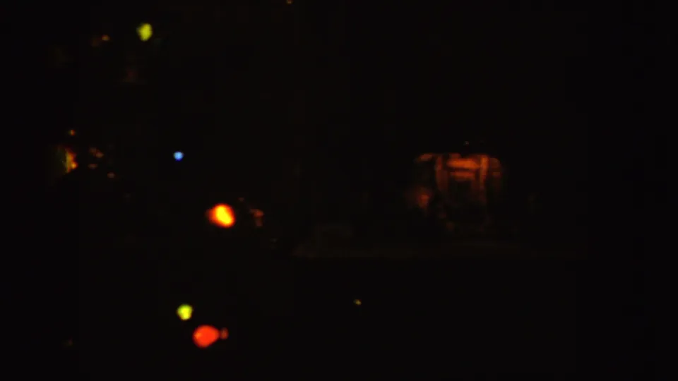 Dim 1955 Idaho home-movie frame showing faint furniture forms and small colored Christmas lights in shadow.