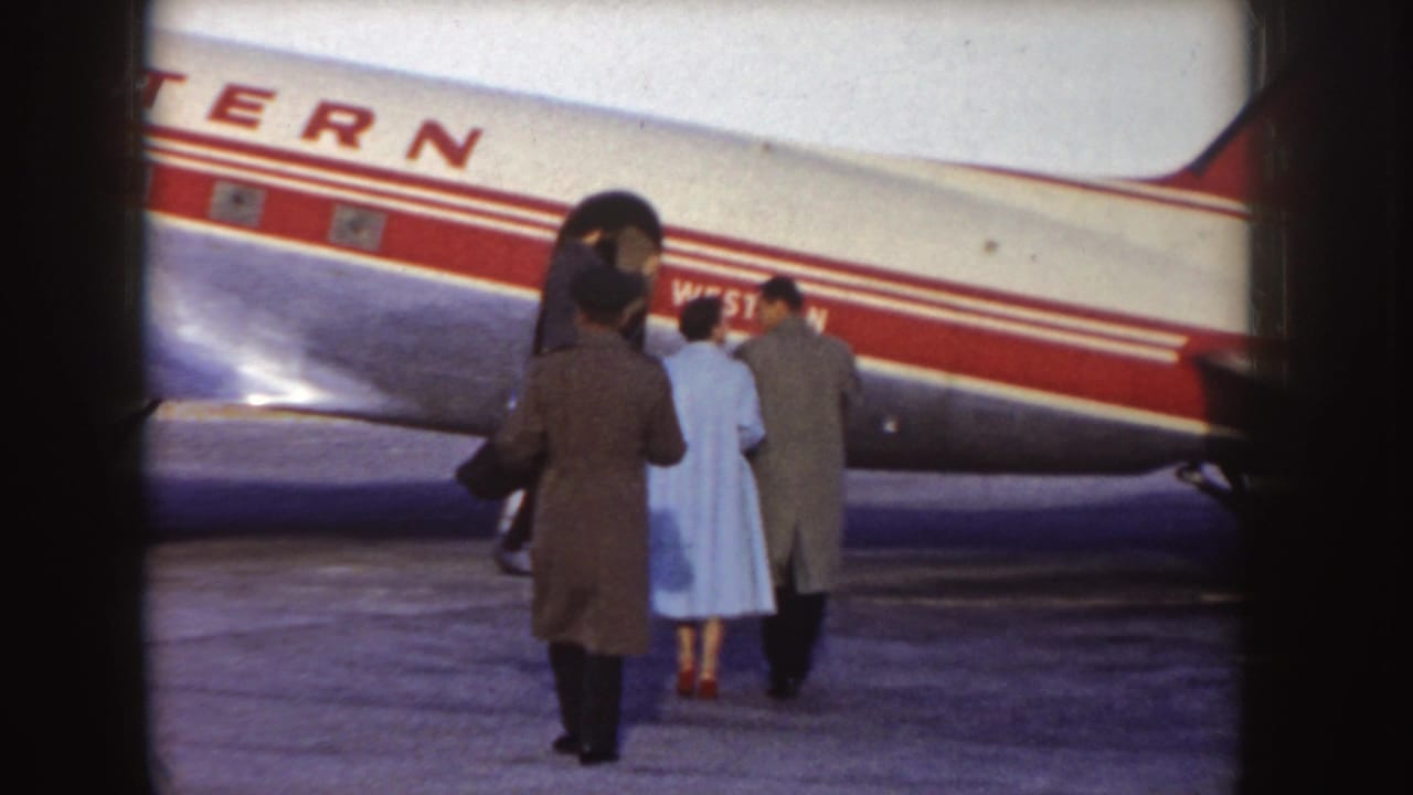 In Idaho 1955 home-movie footage, bundled passengers walk across the tarmac toward the open door of a Western Airlines DC-3-style propeller airliner.