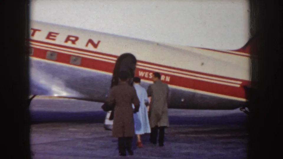 Passengers in coats gather near the open door of a Western Airlines aircraft on an Idaho tarmac in the supplied 1955 metadata context.