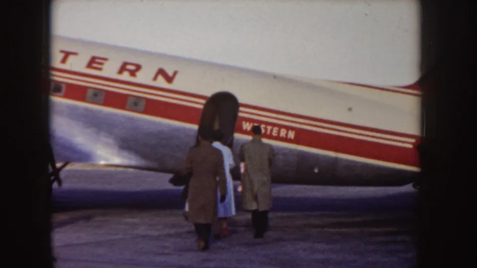 A handheld 8mm frame shows passengers moving toward the open door of a Western Airlines propeller airliner, with the red livery stripe prominent along the fuselage.