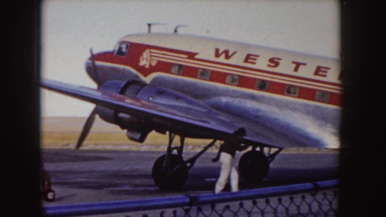 1955 Idaho frame showing the side of a Western Airlines propeller aircraft on the tarmac as a ground crew member walks beside the wing and landing gear.