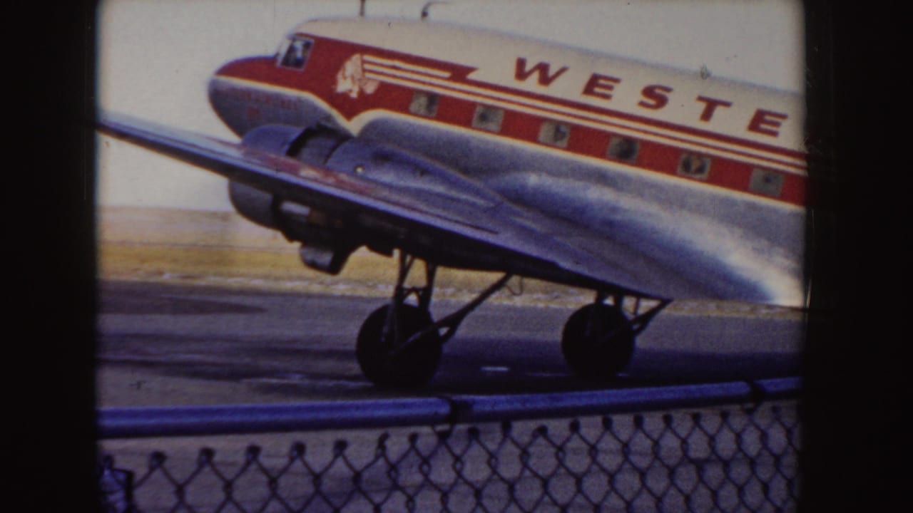 1955 Idaho home-movie frame showing the nose and wing of a Western Airlines DC-3 taxiing behind an airport fence.