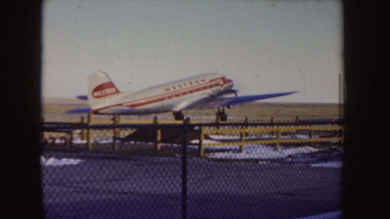 Western Airlines propeller plane on a snowy runway behind a chain-link fence.