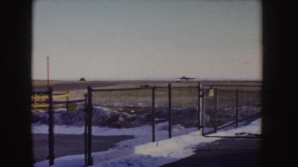 The aircraft is small in the distance on the Idaho airfield, with snowy ground, perimeter fencing, and a pale winter sky visible.