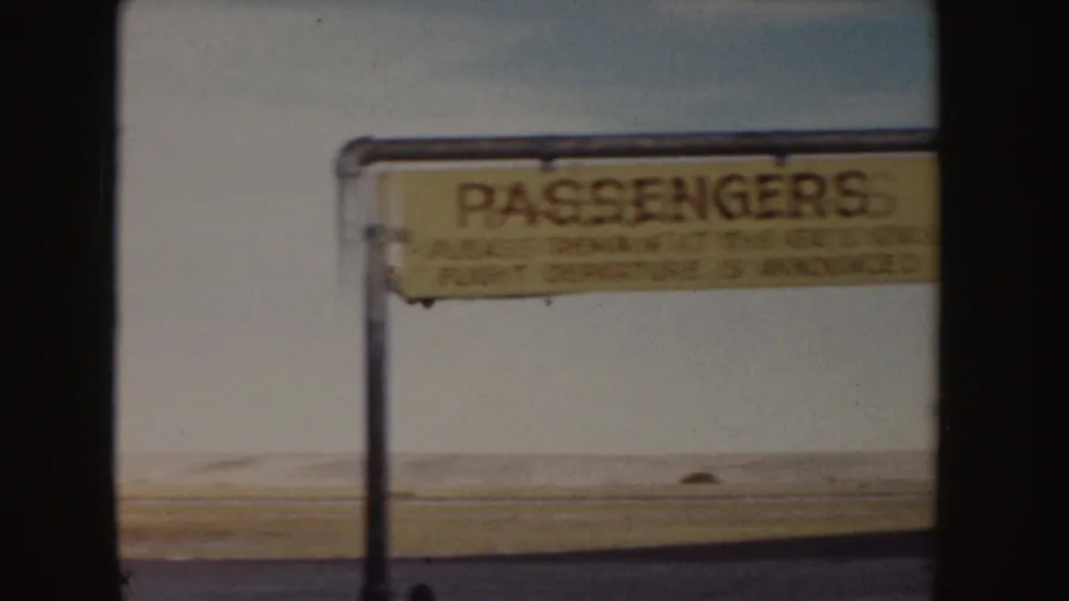 Airport passenger sign stands beside the open airfield after the small plane has moved out of view in this 1955 Idaho home-movie frame.