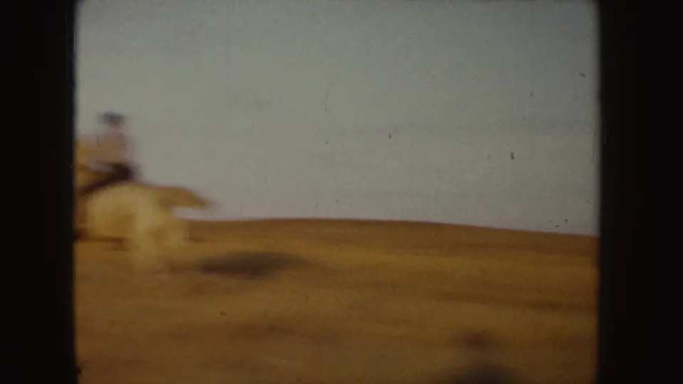 Motion-blurred 1955 Idaho 8mm frame showing a horseback rider moving through a tan field under open sky.