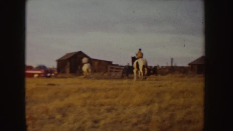 1955 Idaho ranch view with a rider on a white horse moving toward a barn and fence line.
